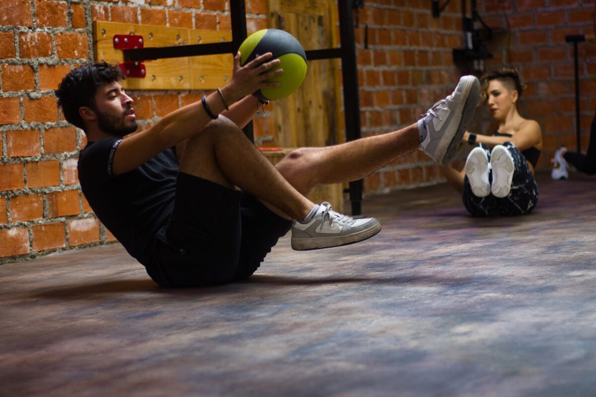 A man and woman perform core exercises with a medicine ball in a brick wall gym.