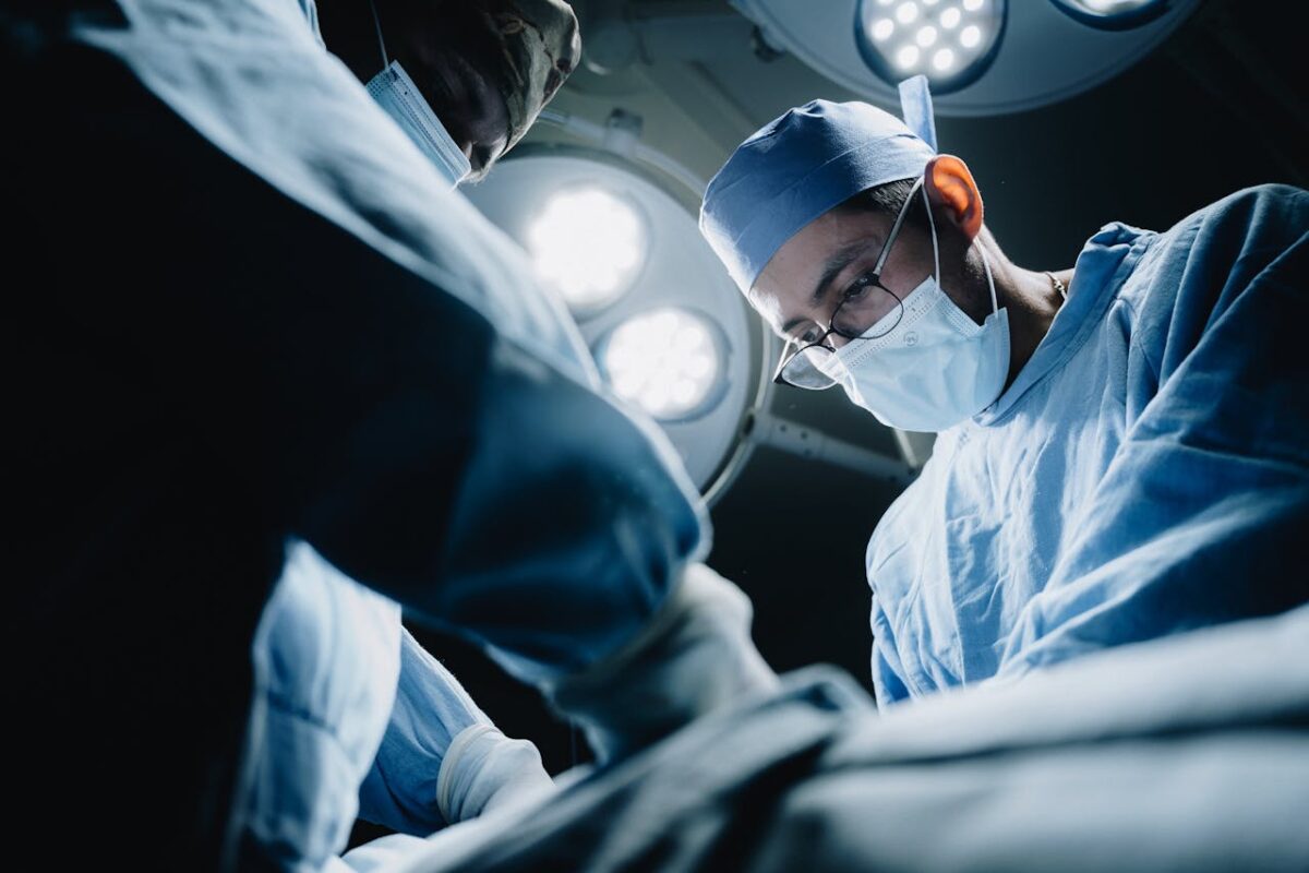 Doctors in surgical attire focus on an operation under bright lights in a modern operating room.